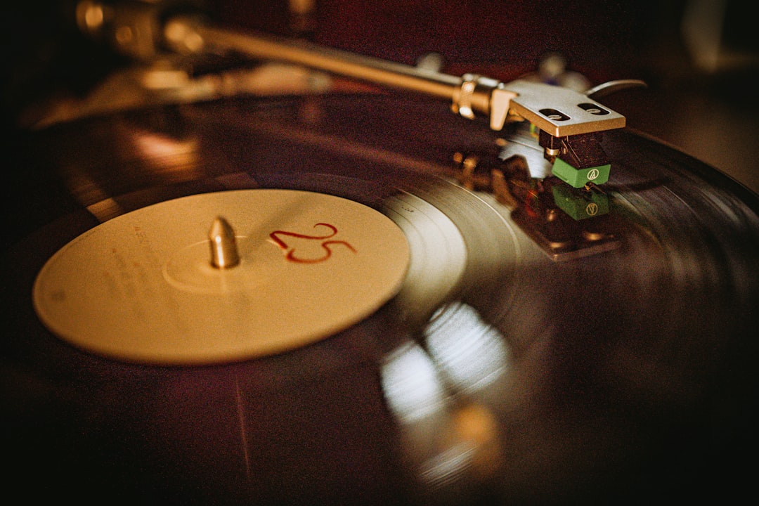 A turntable tonearm positioned over a spinning vinyl record on a wooden surface