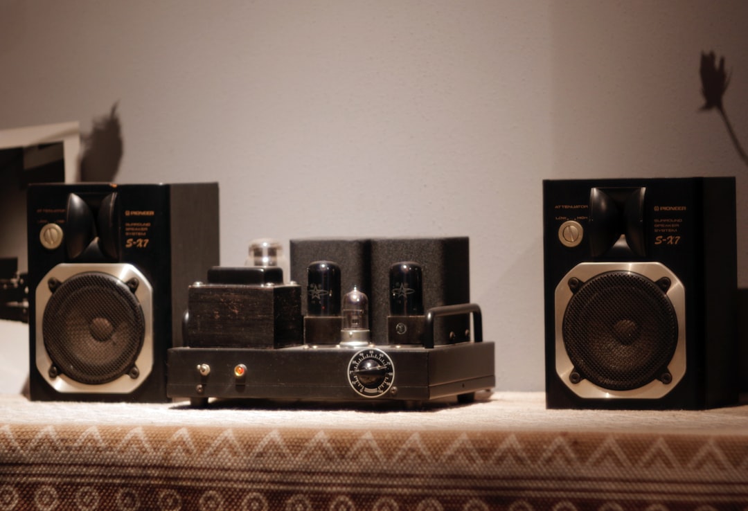 Two stereo speakers flanking a vintage vacuum tube amplifier on a wood shelf
